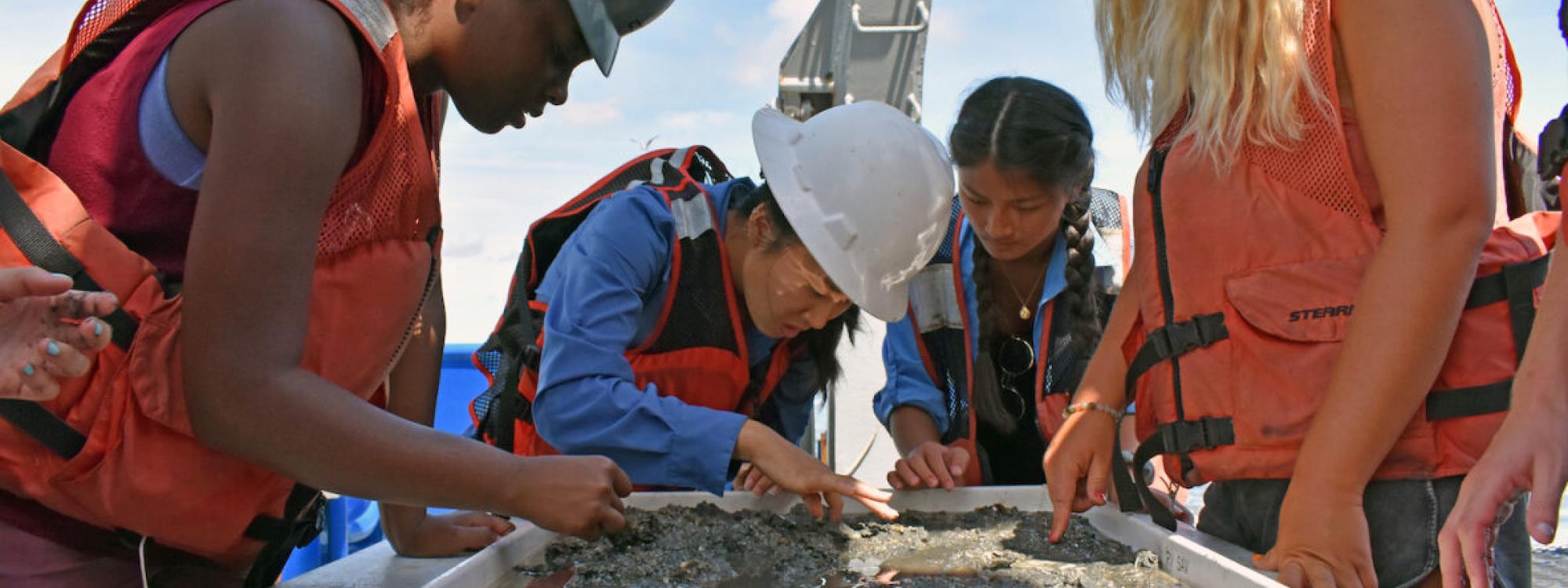 Four students in life jackets sift through marine sediment 