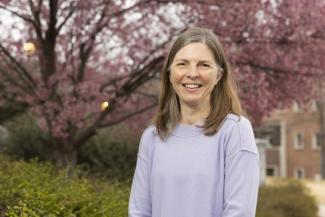 Dr. Erin Dolan smiles widely into the camera. She is wearing a soft lilac sweater and he face is framed by mousy brown shoulder length hair.