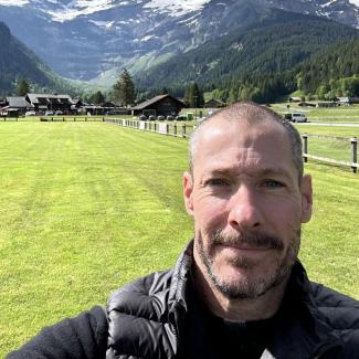 Dr. Cameron Thrash smiles in a selfie backed by a mountain range