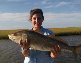 Dr. Ziegler stands center frame smiling and holding a large red drum fish