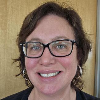 Dr. Gretchen Mullendore smiles in a headshot with slightly boxy glasses and shoulder length hair. 