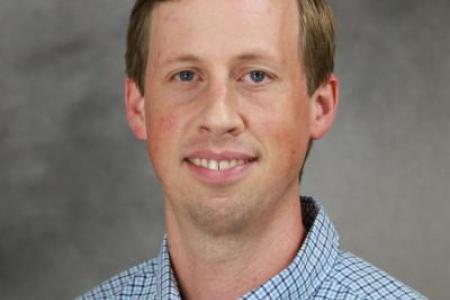 A head shot of Dr. Adam Greer in a blue and white checkered button up. 