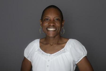 Dr. Erica Holloman Hill smiles at the camera in light white shirt that compliments her dark skin. Her hair is short and she sports large silver hoop earrings