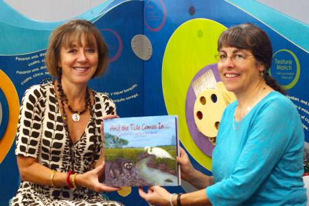 State Librarian Julie Walker, left, and University of Georgia marine sciences professor Merryl Alber hold up “And the Tide Comes In,” a children’s book on salt marshes now available at every public library in the state