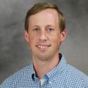 A head shot of Dr. Adam Greer in a blue and white checkered button up. 