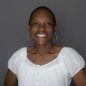 Dr. Erica Holloman Hill smiles at the camera in light white shirt that compliments her dark skin. Her hair is short and she sports large silver hoop earrings